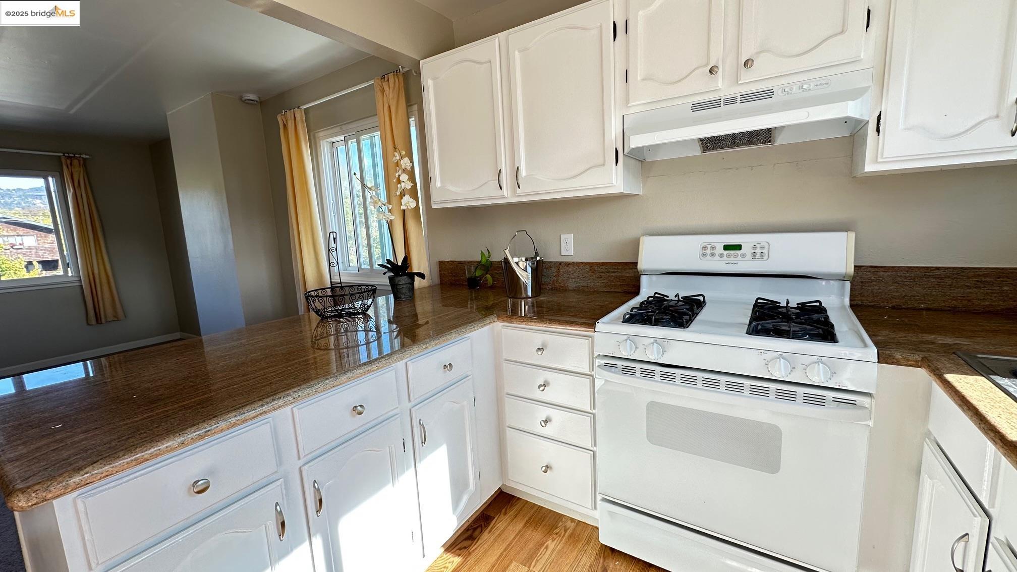 840 Key Rte Boulevard Albany, CA 94706 - Photo 18 of 29 Kitchen featuring white range with gas cooktop, white cabinetry, under cabinet range hood, and light wood-style flooring