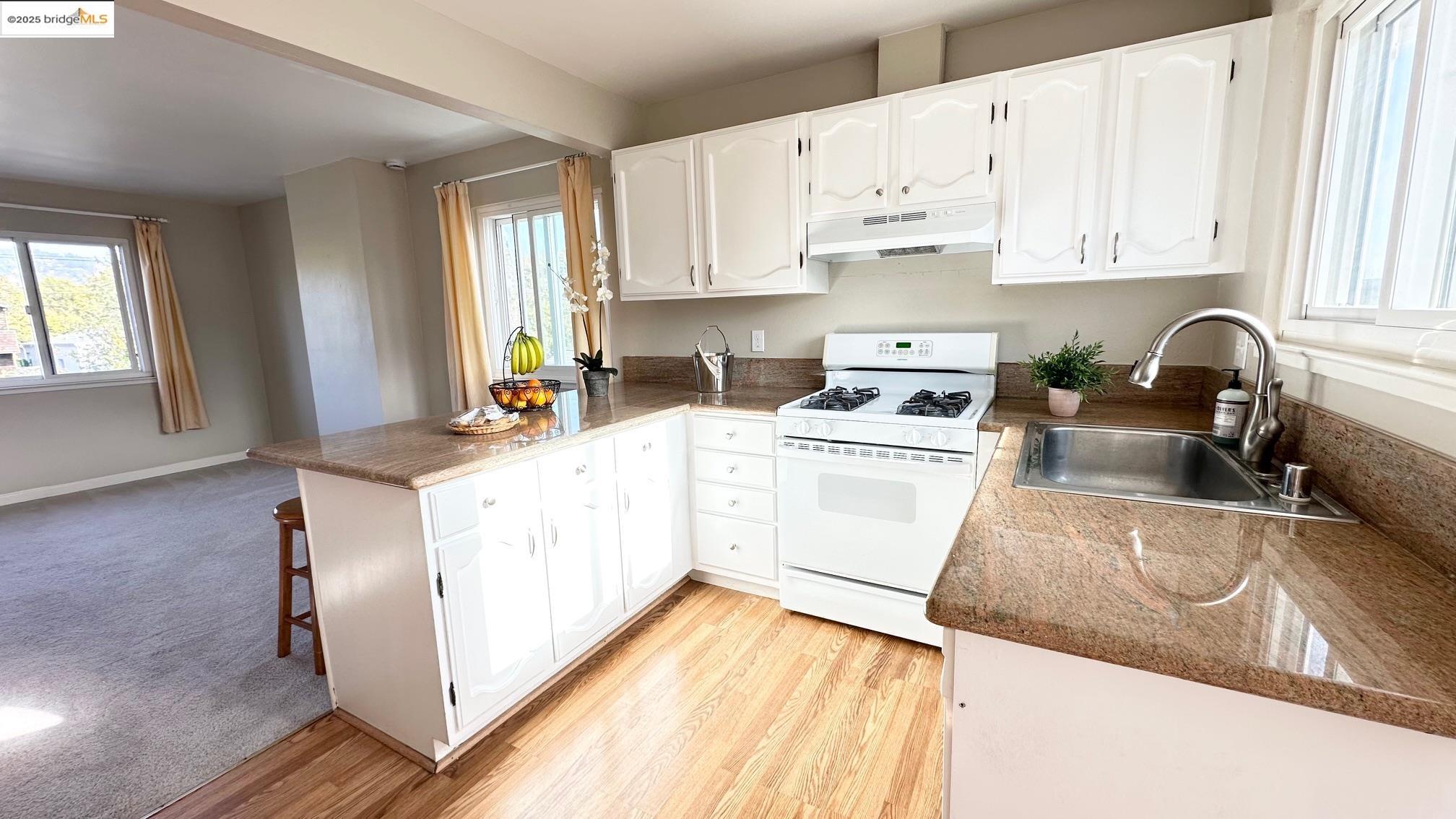 840 Key Rte Boulevard Albany, CA 94706 - Photo 19 of 29 Kitchen with plenty of natural light, white gas stove, a peninsula, and white cabinetry