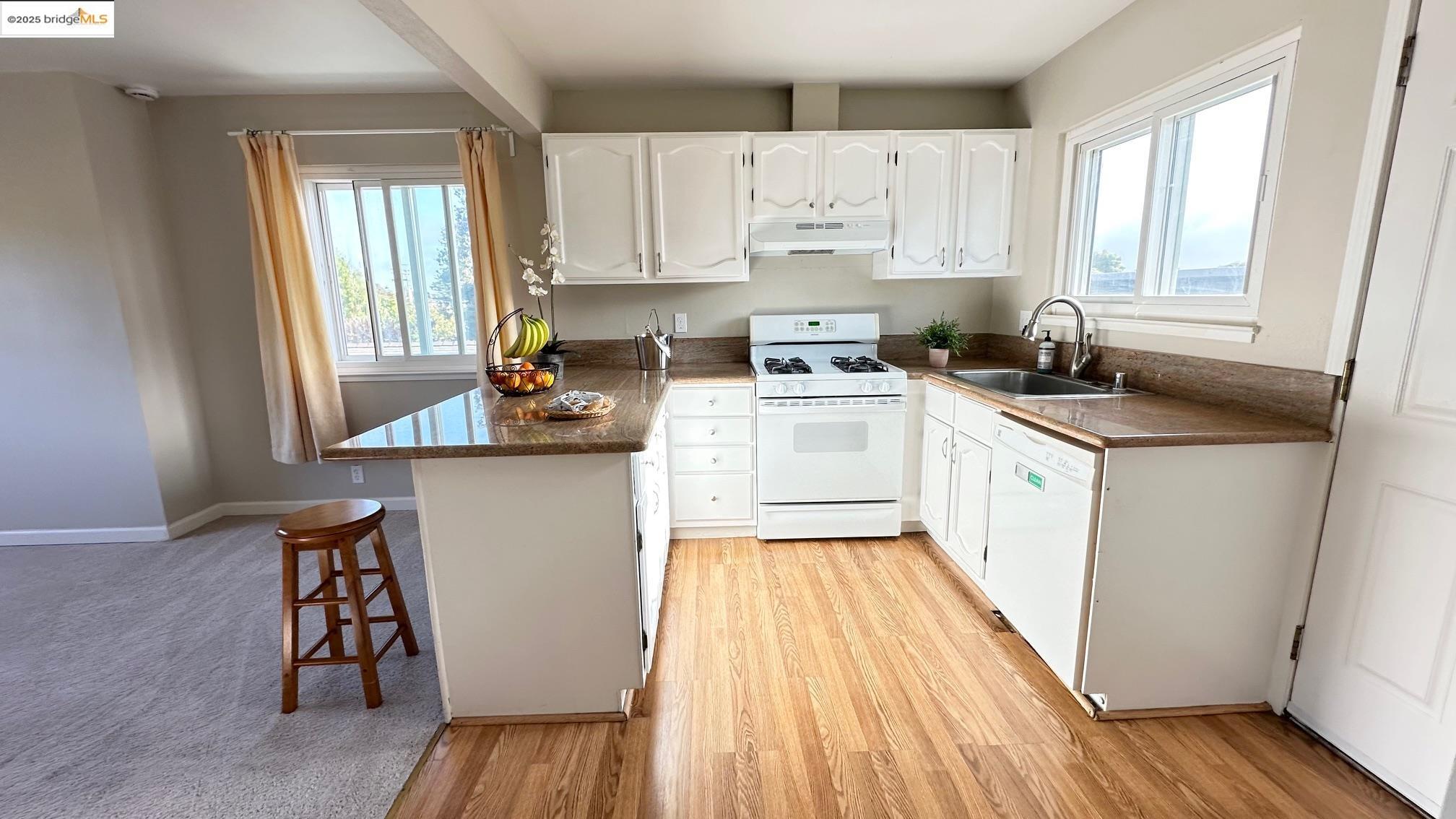 840 Key Rte Boulevard Albany, CA 94706 - Photo 21 of 29 Kitchen featuring a peninsula, a kitchen breakfast bar, white appliances, white cabinets, and under cabinet range hood