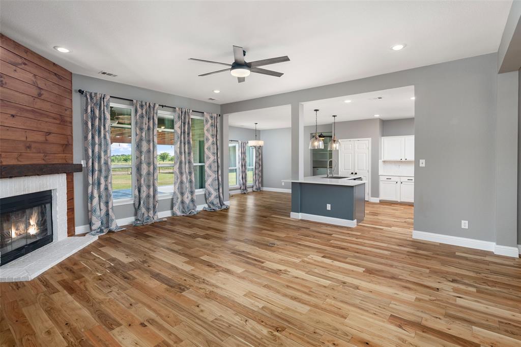 1019 Vaughan Lane Tioga, TX 76271 - Photo 8 of 40 Open-concept living area featuring wood-finish flooring, a fireplace with a white tile hearth, and a wood-paneled accent wall