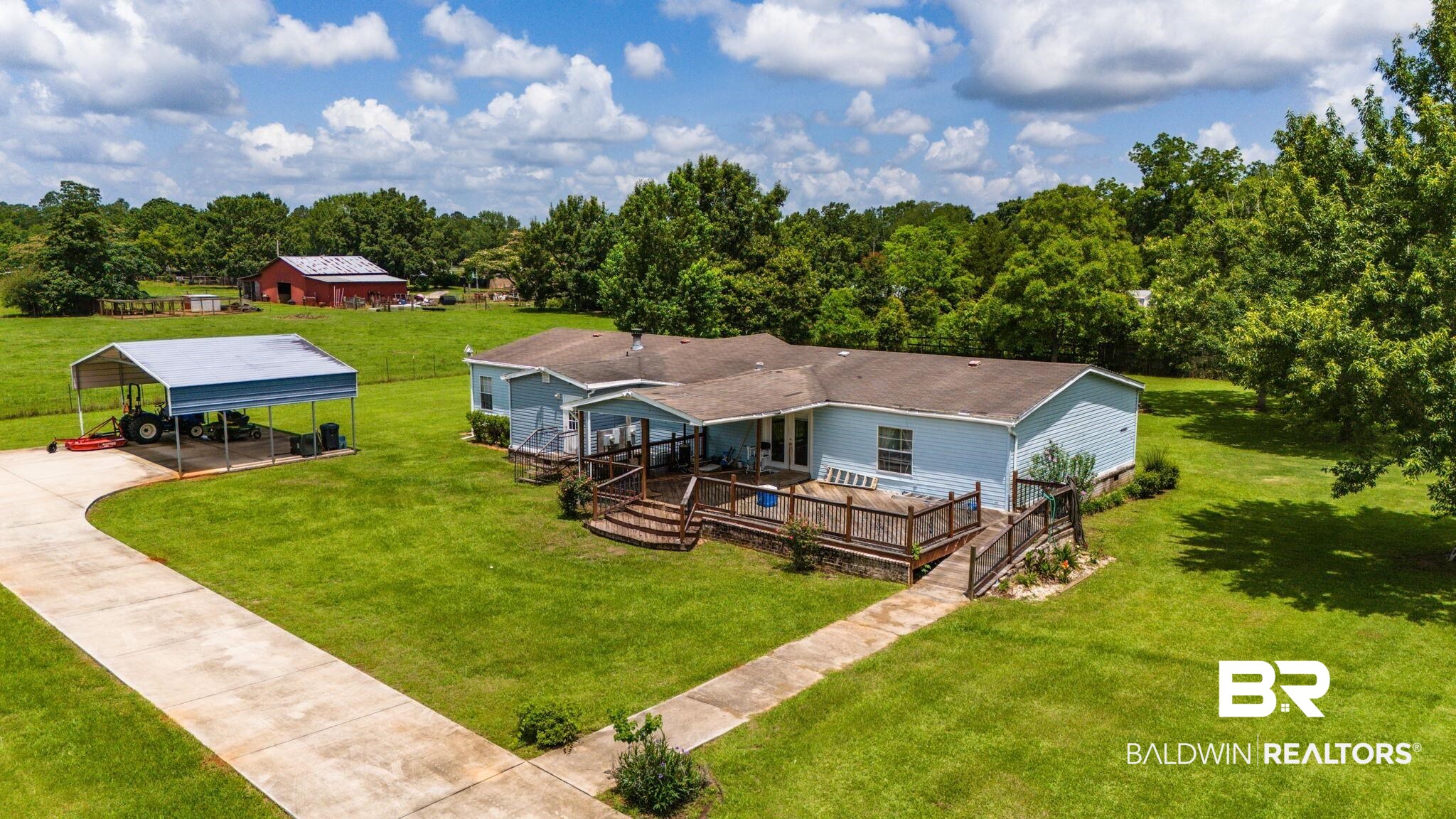 34985b Spring Road South, Unit B Stapleton, AL 36578 - Photo 3 of 31 Light blue exterior home with a sprawling front lawn, featuring a concrete driveway, a separate covered carport structure, and a large wooden deck with railing