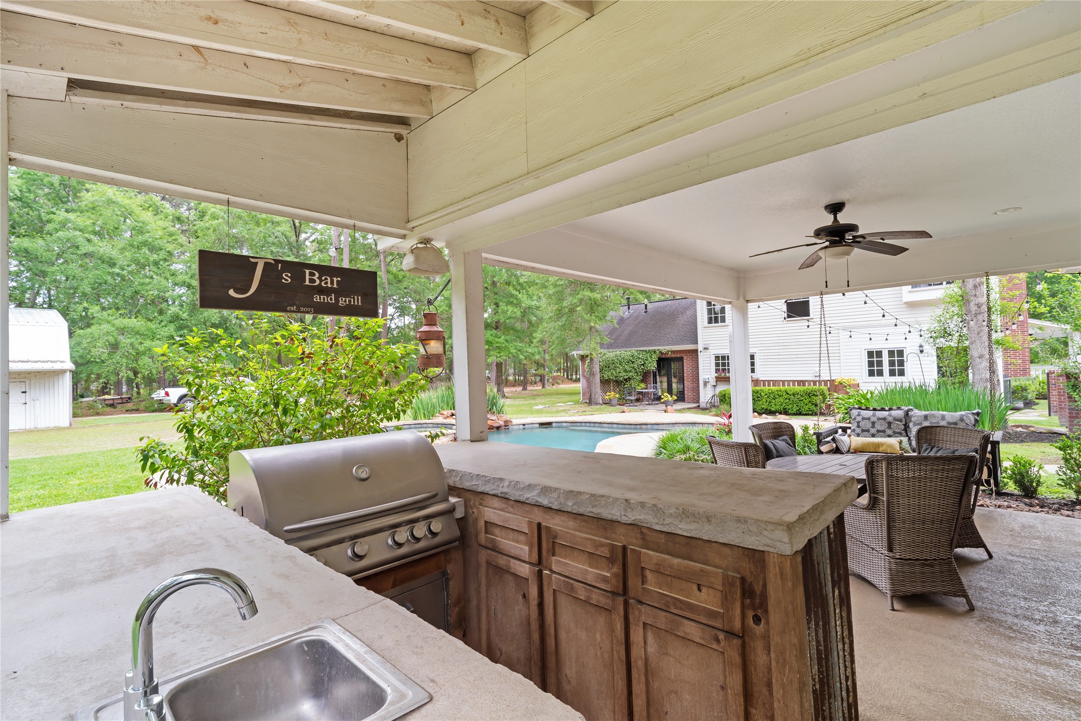 36 Wind River Drive Conroe, TX 77384 - Photo 37 of 45 This photo showcases a charming outdoor living space with a covered patio, featuring a built-in grill and bar area. It overlooks a pool and lush backyard, perfect for entertaining and relaxing.