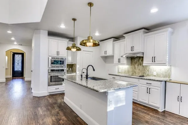 a kitchen with stainless steel appliances granite countertop a sink a stove and a wooden floors