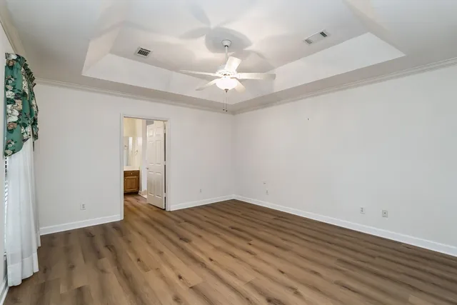 an empty room with wooden floor chandelier fan and windows