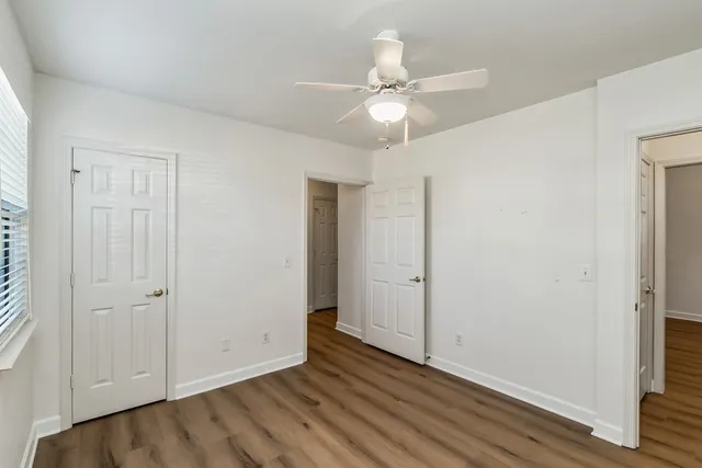 an empty room with wooden floor fan and windows