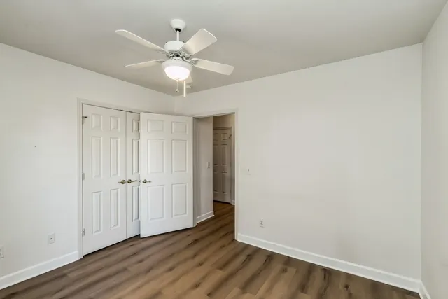 an empty room with wooden floor fan and windows