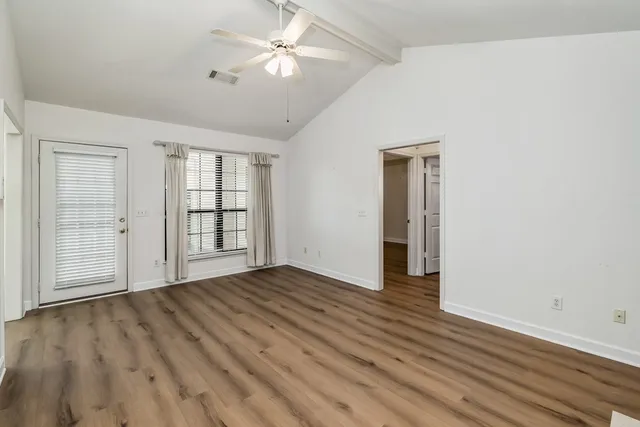 an empty room with wooden floor chandelier fan and windows