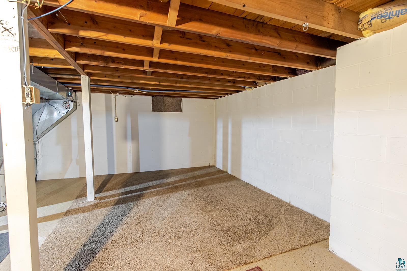 7045 Morris Thomas Road Cloquet, MN 55720 - Photo 22 of 28 Unfinished basement space featuring exposed wood joists and support beams, white block walls, and existing carpet flooring