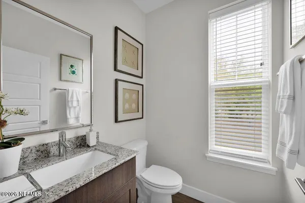 a bathroom with a granite countertop toilet a sink a mirror and a window