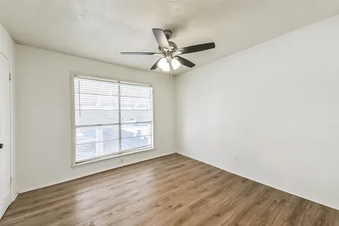 an empty room with wooden floor chandelier fan and windows