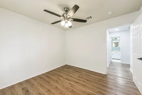 an empty room with wooden floor fan and windows