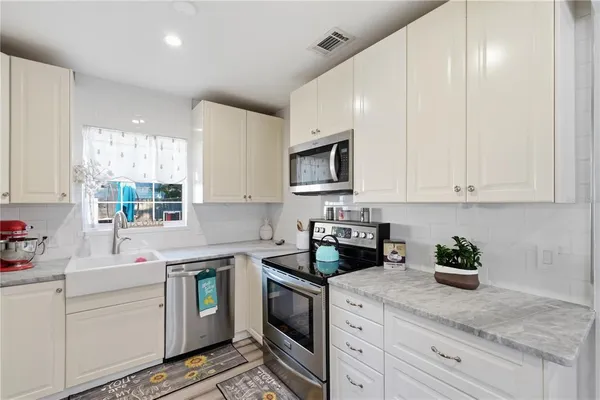 a kitchen with white cabinets appliances a sink and a window