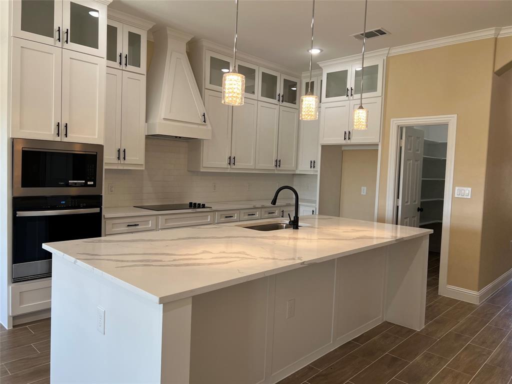 7363 Northeast County Road Rice, TX 75155 - Photo 2 of 4 Kitchen featuring a large central island with a stone countertop, white shaker cabinetry, stainless steel built-in appliances, and a tile backsplash
