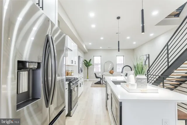 a kitchen with stainless steel appliances kitchen island granite countertop a refrigerator a sink a oven and a dining table with wooden floor