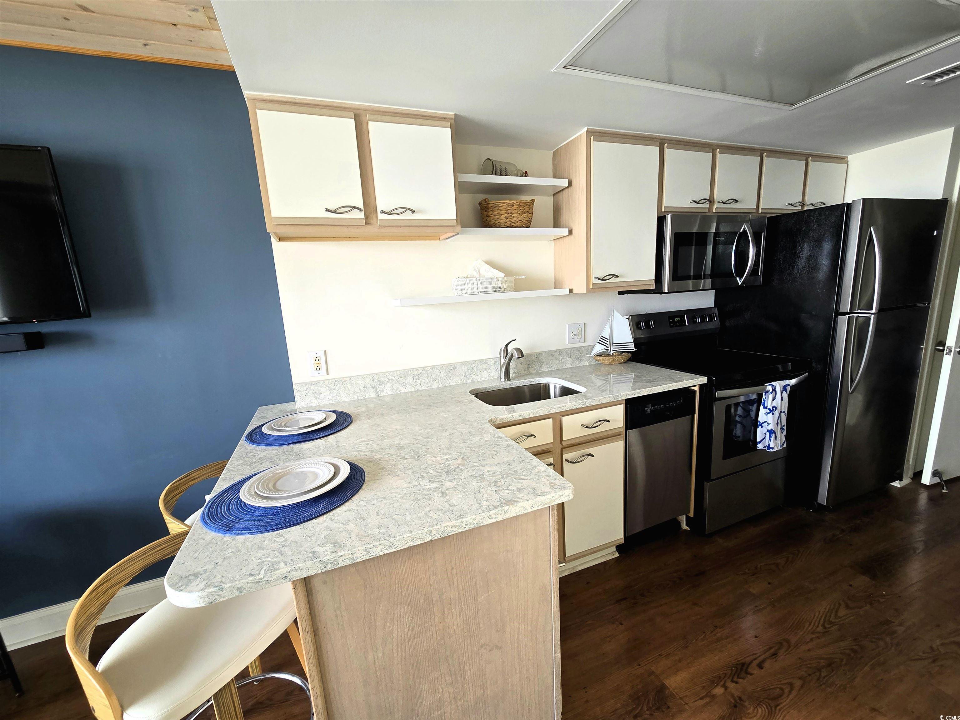 161 Seawatch Drive, Unit 414 Myrtle Beach, SC 29572 - Photo 7 of 15 Kitchen with open shelves, stainless steel appliances, a kitchen bar, and dark wood-style floors