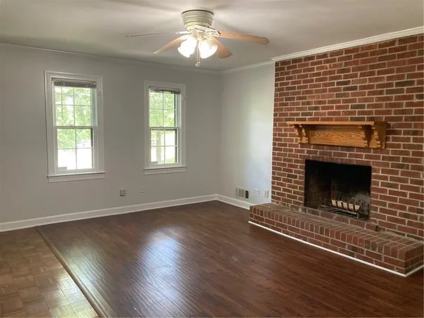 an empty room with wooden floor fireplace cabinet and windows