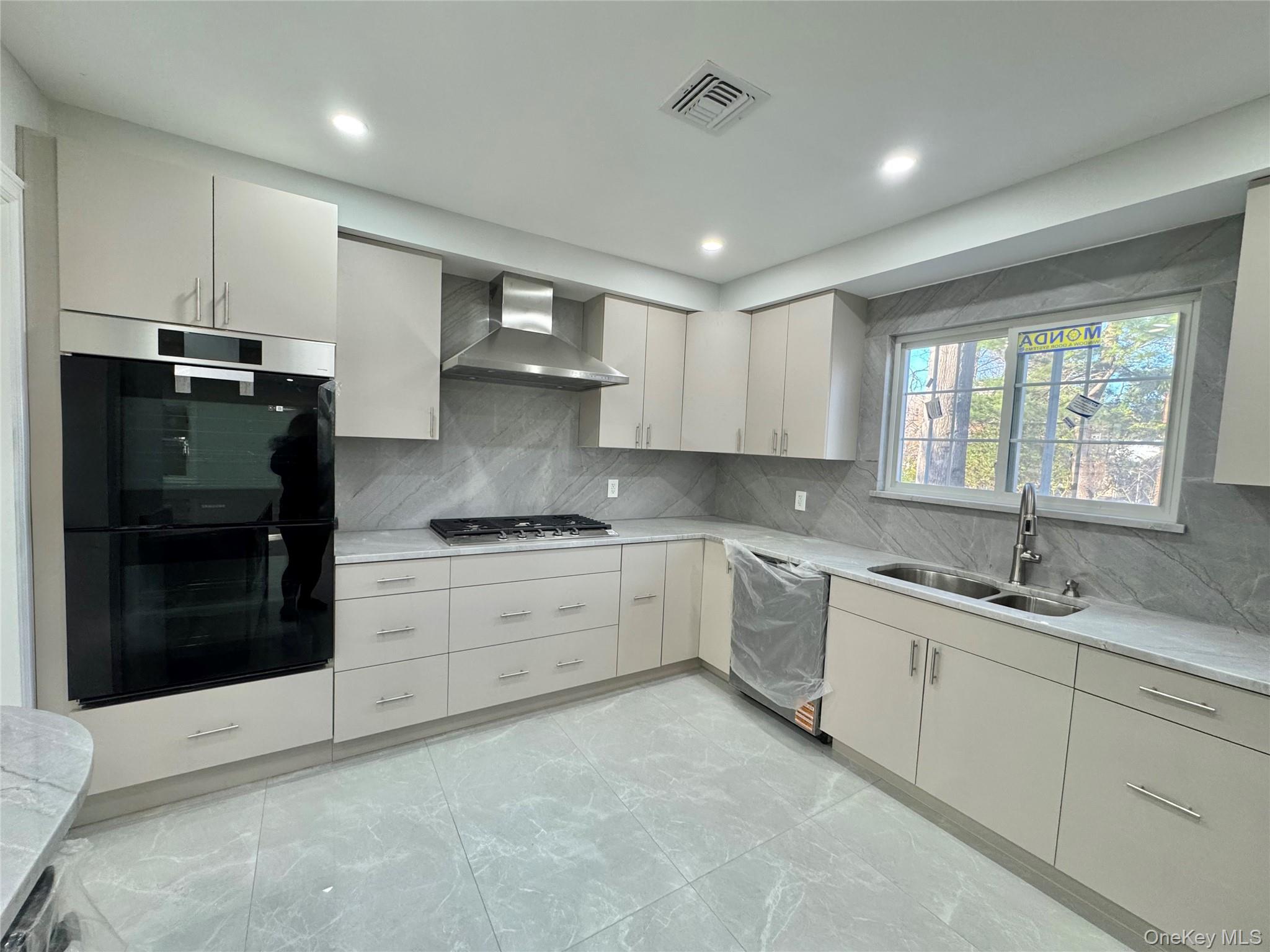 32 A Berkshire Road Great Neck, NY 11023 - Photo 11 of 38 Kitchen featuring appliances with stainless steel finishes, wall chimney range hood, backsplash, light stone counters, and modern cabinets