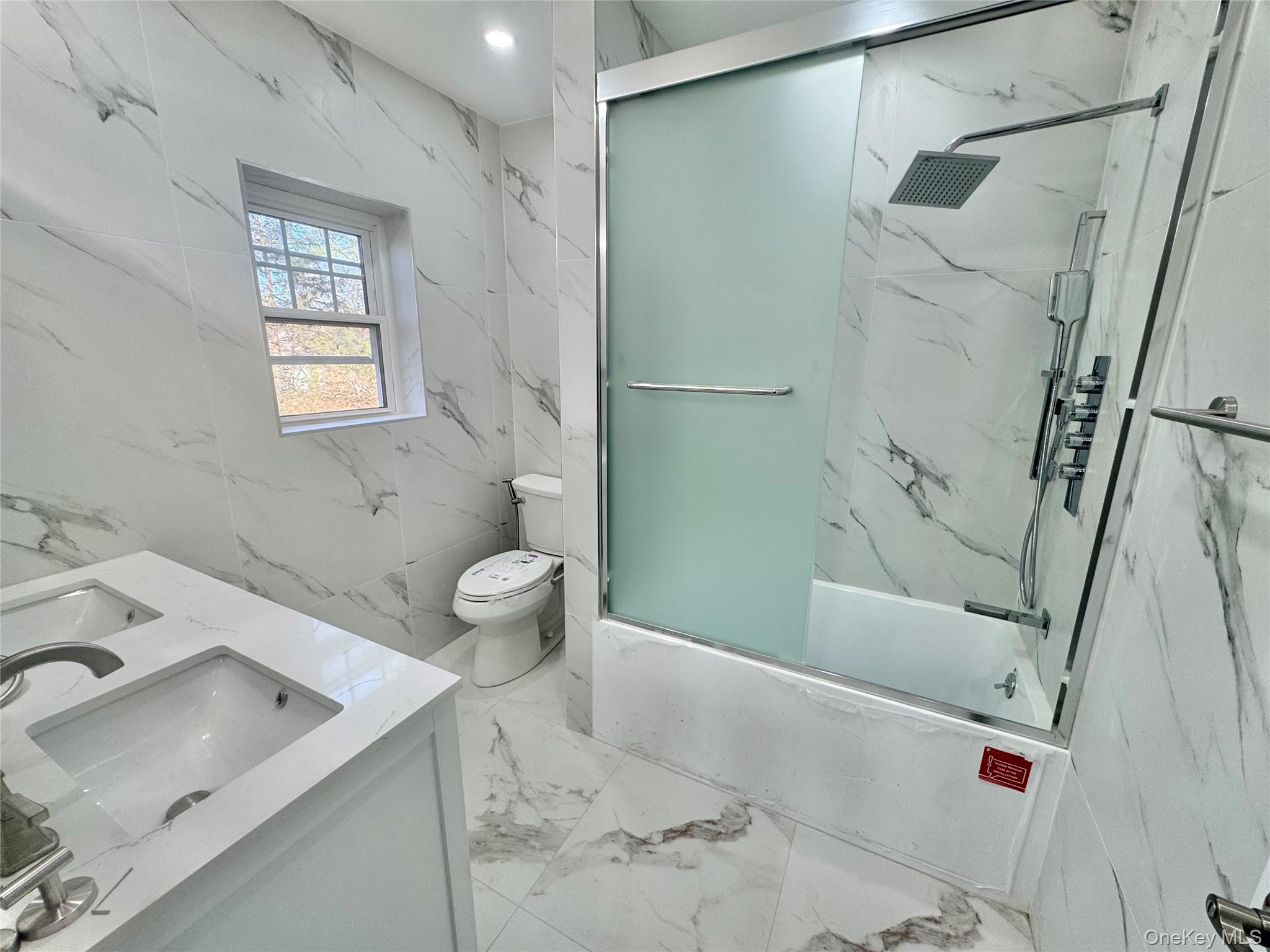 32 A Berkshire Road Great Neck, NY 11023 - Photo 18 of 38 Full bathroom with double vanity, enclosed tub / shower combo, light marble finish floors, stone wall, and tile walls, window and fan