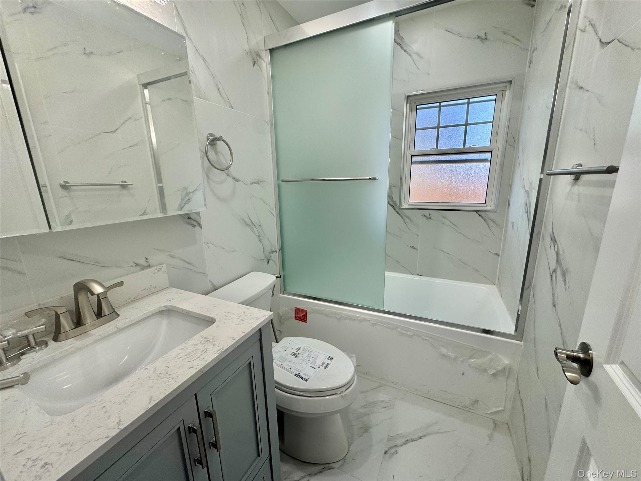 32 A Berkshire Road Great Neck, NY 11023 - Photo 21 of 38 Full bath with marble tiled floors, vanity, bath / shower combo with glass door, stone wall, and tile walls