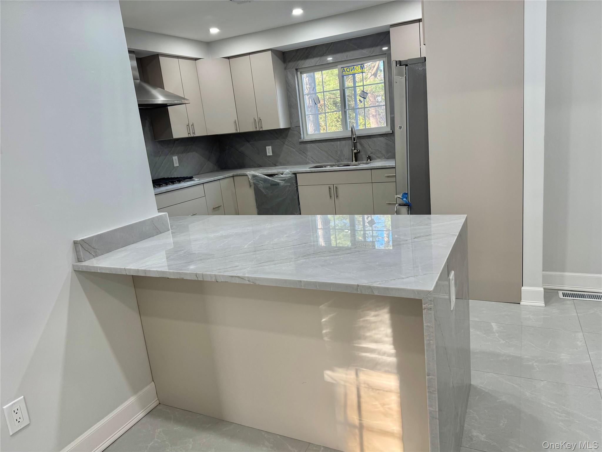 32 A Berkshire Road Great Neck, NY 11023 - Photo 25 of 38 Kitchen featuring a peninsula, light stone counters, stainless steel appliances, backsplash, and white cabinetry