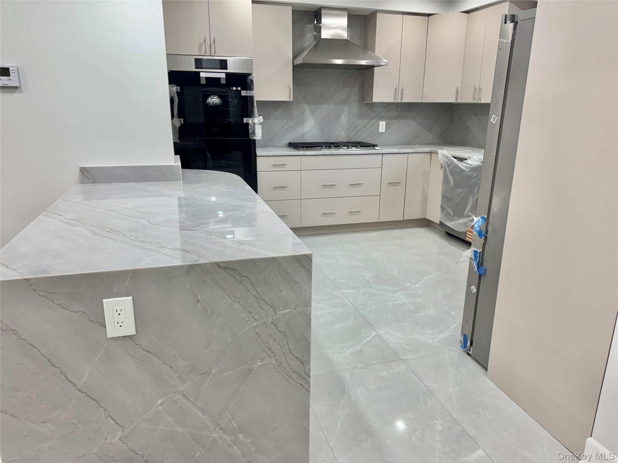 32 A Berkshire Road Great Neck, NY 11023 - Photo 26 of 38 Kitchen featuring light stone countertops, light marble finish flooring, backsplash, wall chimney range hood, and appliances with stainless steel finishes