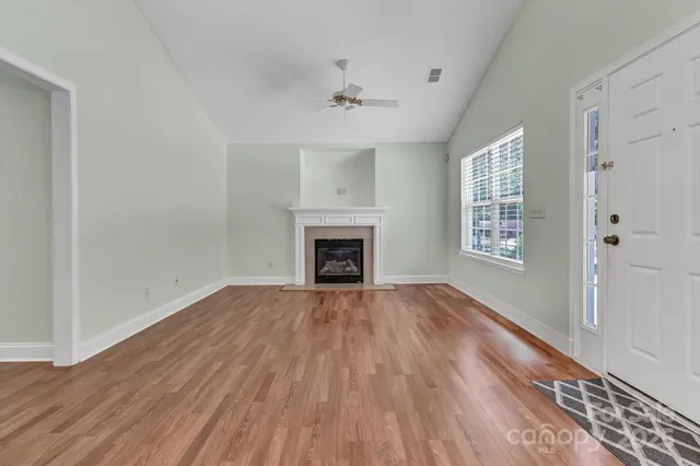 a view of an empty room with wooden floor fireplace and a window