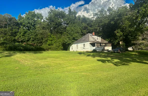 a white house with a big yard plants and large trees