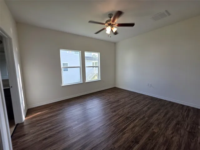 an empty room with wooden floor chandelier fan and windows