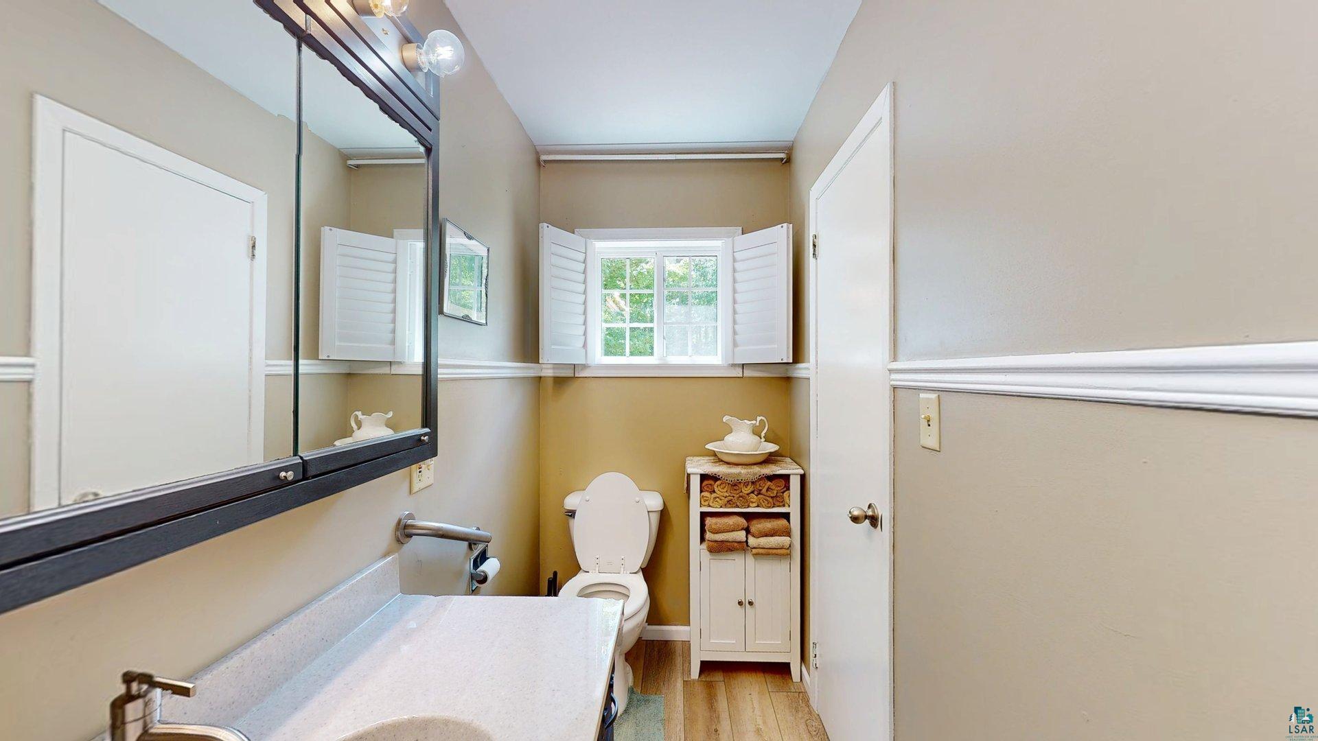 10614 Moose Lake Road Orr, MN 55771 - Photo 21 of 44 Bathroom featuring wood-finish flooring, a vanity with an integrated sink, a wall-mounted medicine cabinet with integrated lighting, a window with white shutters, and chair rail molding