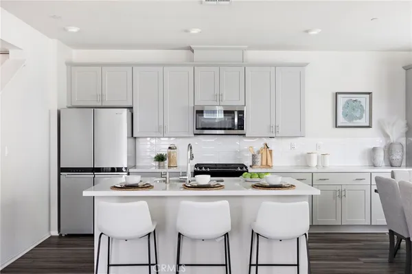 a kitchen with stainless steel appliances a sink a stove a refrigerator with white cabinets and wooden floor