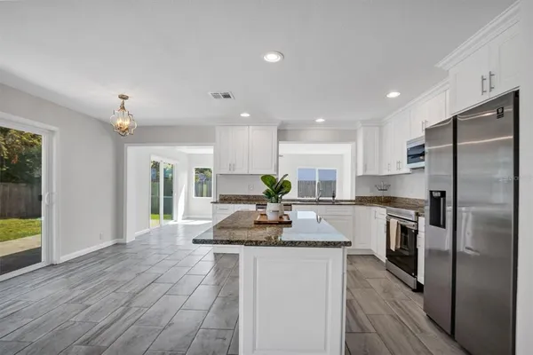 a kitchen with kitchen island granite countertop a stove a sink a refrigerator and white cabinets with wooden floor