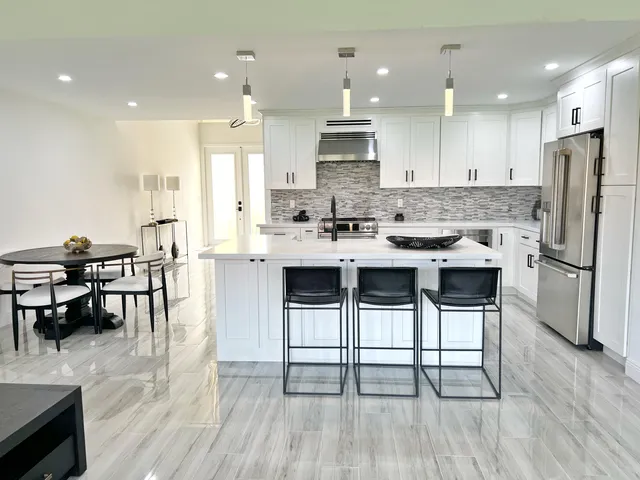 a kitchen with stainless steel appliances kitchen island granite countertop a dining table chairs and white cabinets