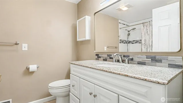 a bathroom with a granite countertop sink vanity mirror and toilet