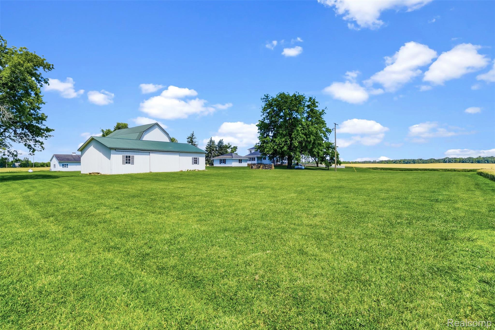 5843 West Dewey Road Owosso, MI 48867 - Photo 44 of 58 Expansive green lawn with a large white barn featuring a green metal roof and multiple windows