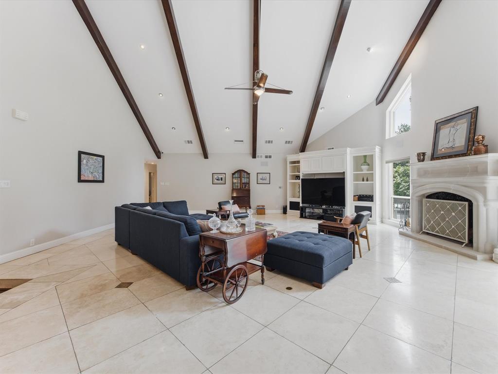 6160 Spring Valley Road Dallas, TX 75240 - Photo 18 of 40 Spacious living area featuring a vaulted ceiling with exposed wood beams, a stone fireplace, built-in shelving, and large format tile flooring