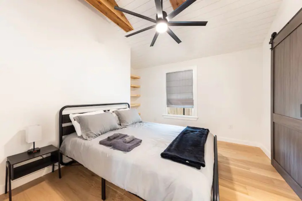 2319 Santa Rita Street Austin, TX 78702 - Photo 8 of 26 Bedroom featuring a barn door, light wood-style floors, vaulted ceiling with beams, and ceiling fan