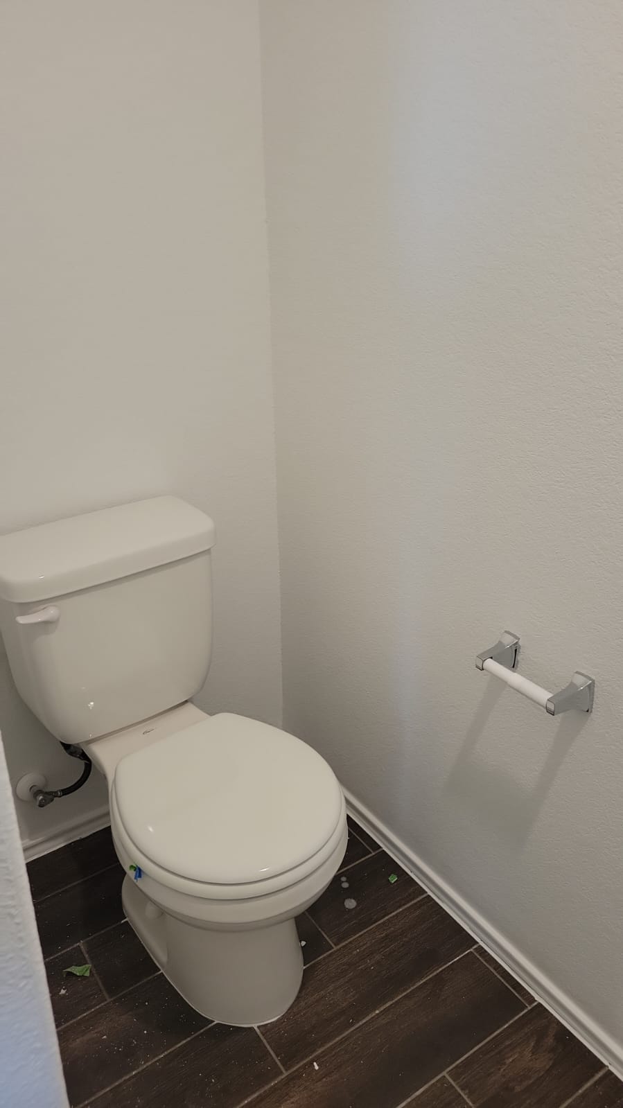 541 Pickrell Loop Georgetown, TX 78628 - Photo 25 of 32 A white toilet with a toilet paper holder, set against white walls and dark wood-look flooring