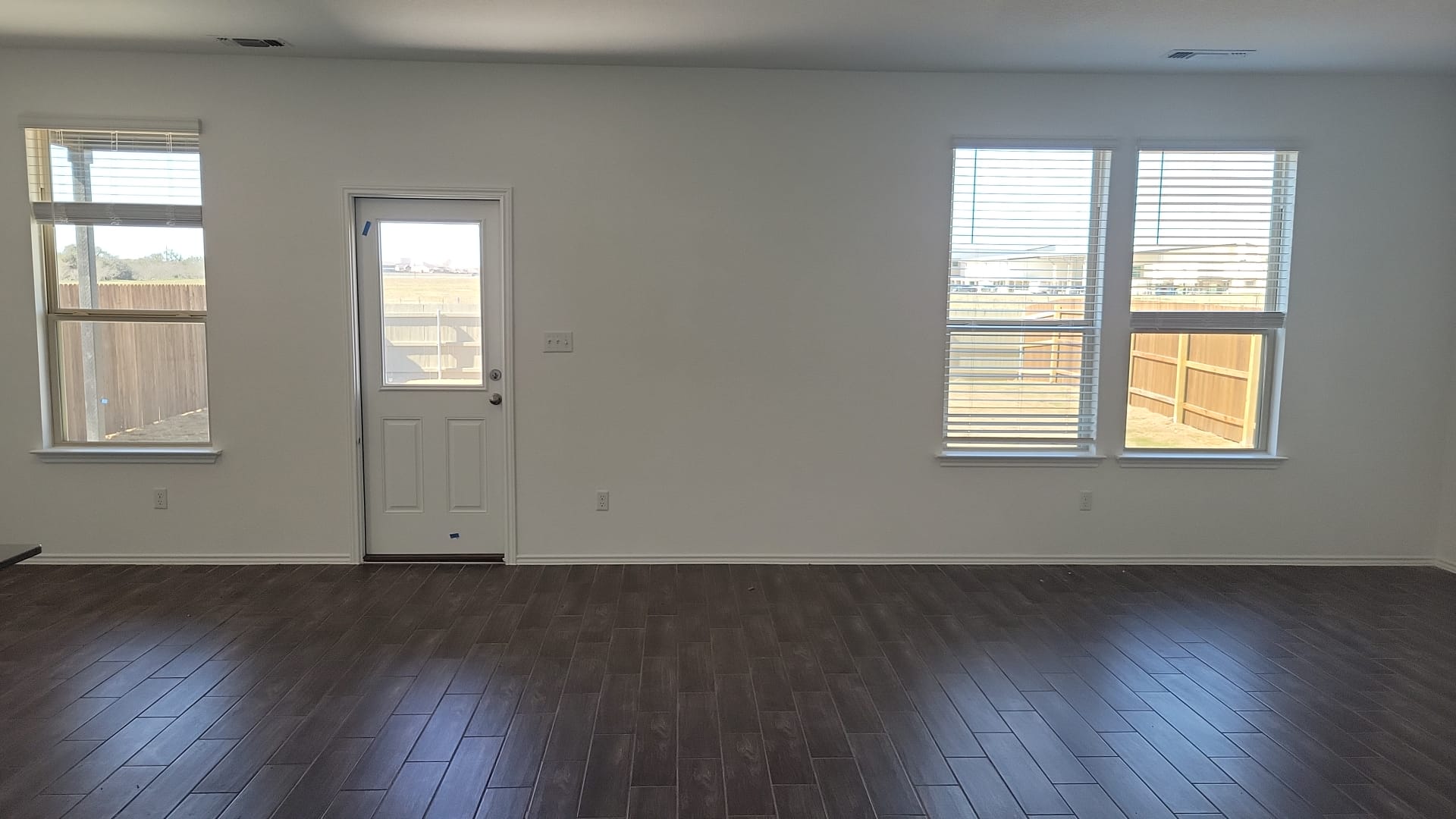 541 Pickrell Loop Georgetown, TX 78628 - Photo 3 of 32 Spacious room featuring dark wood-look flooring, light-colored walls, and multiple windows with blinds, providing natural light