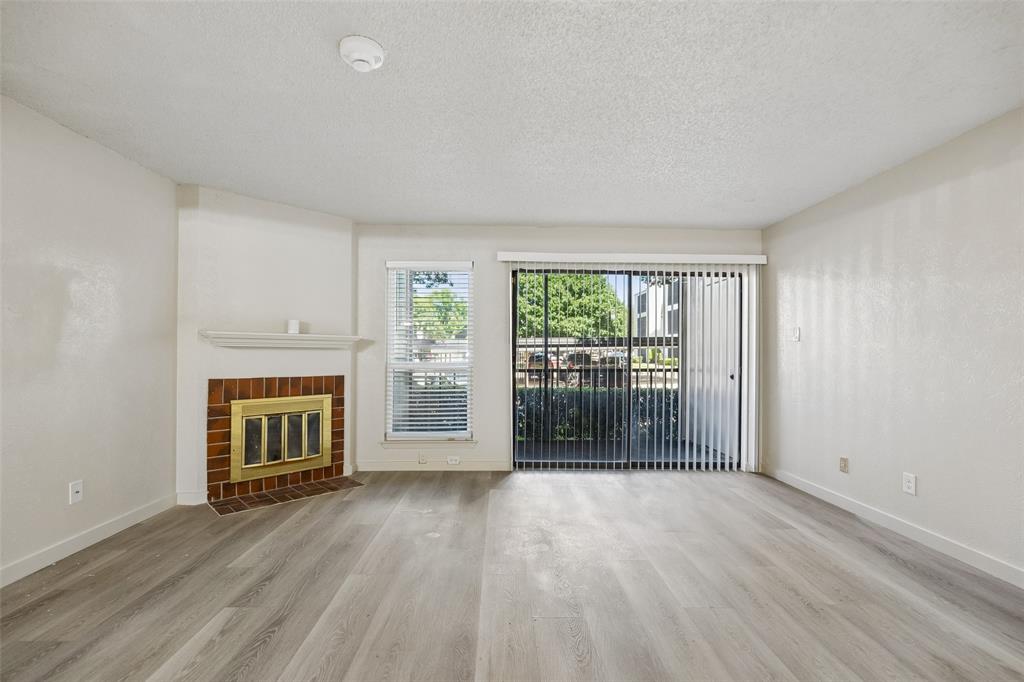 11480 Audelia Road, Unit 136 Dallas, TX 75243 - Photo 4 of 29 Living area featuring light wood-finish flooring, a brick fireplace with a white mantel, and a sliding glass door with vertical blinds