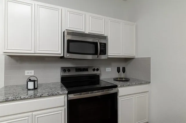 a kitchen with granite countertop white cabinets and a stove top oven