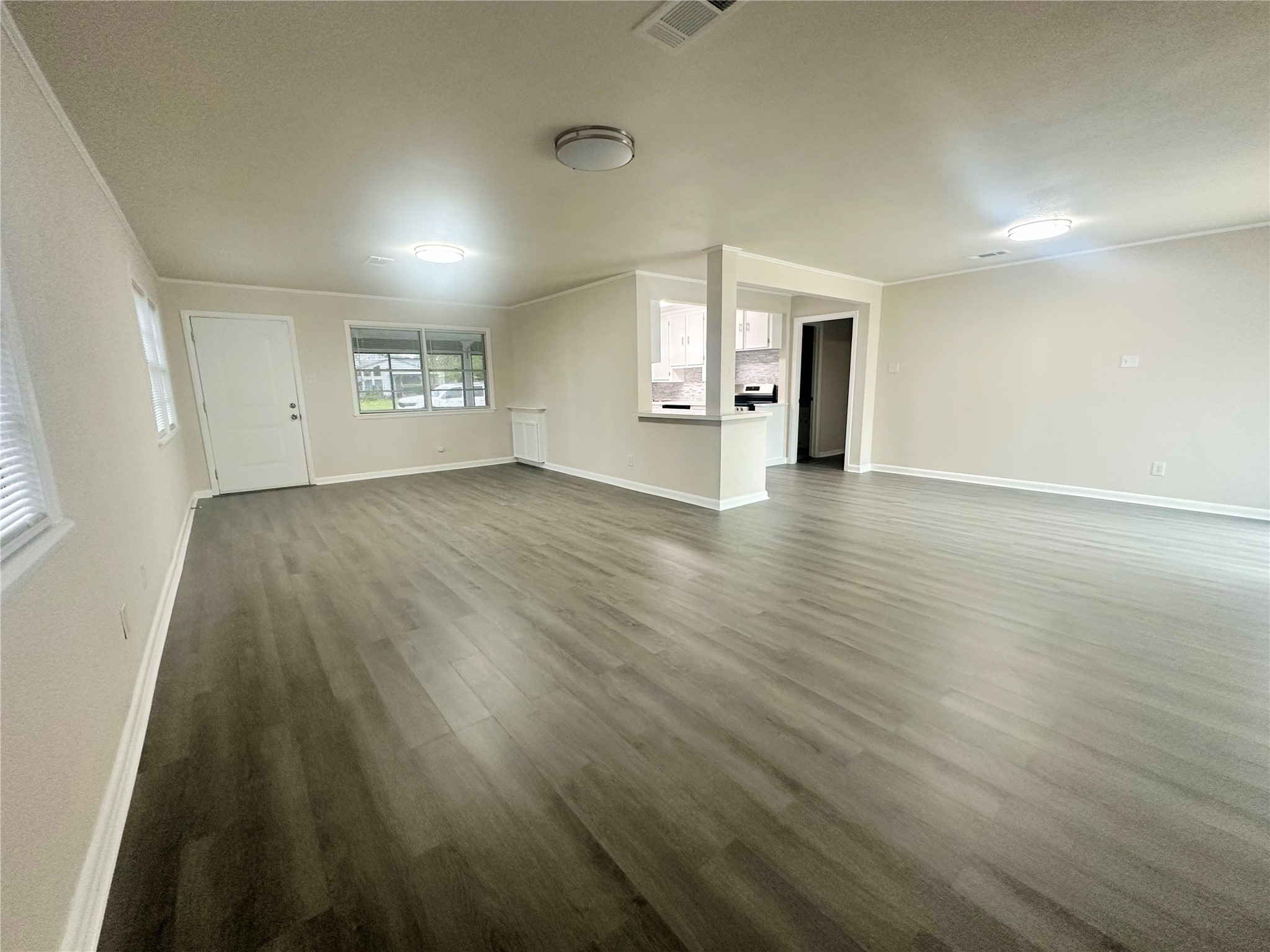 130 Bay Ridge Drive Baytown, TX 77523 - Photo 7 of 20 This photo showcases a spacious, open-plan living area with modern wood-look flooring and neutral walls. It features ample natural light from multiple windows, with a view into the kitchen area, making it ideal for entertaining and family gatherings.