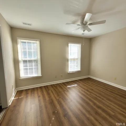 an empty room with wooden floor fan and windows