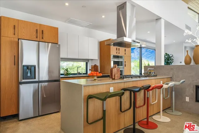 a kitchen with stainless steel appliances granite countertop a refrigerator a sink dishwasher a stove and a dining table with wooden floor