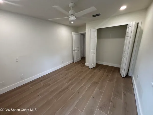 an empty room with wooden floor and a ceiling fan