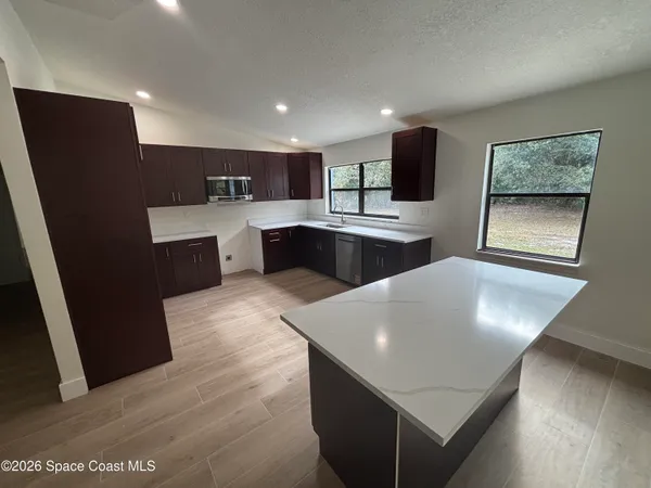 a living room with stainless steel appliances furniture a flat screen tv and view of kitchen
