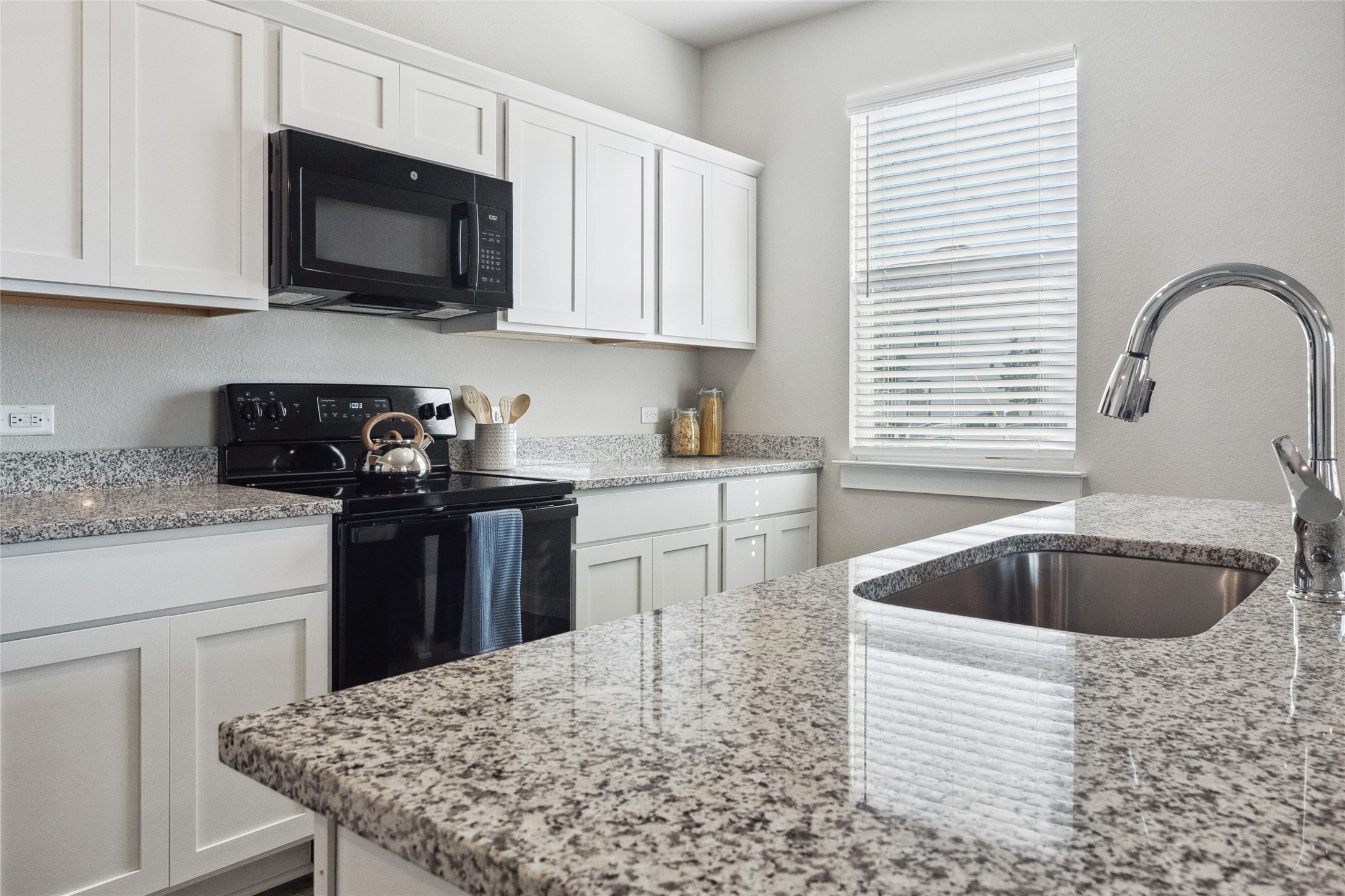 523 Powell Drive, Unit 1101 Leander, TX 78641 - Photo 11 of 24 Kitchen featuring black appliances, white cabinetry, and light stone counters