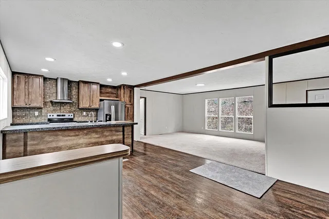 a open kitchen with stainless steel appliances granite countertop a refrigerator a sink a stove and a oven with wooden floors