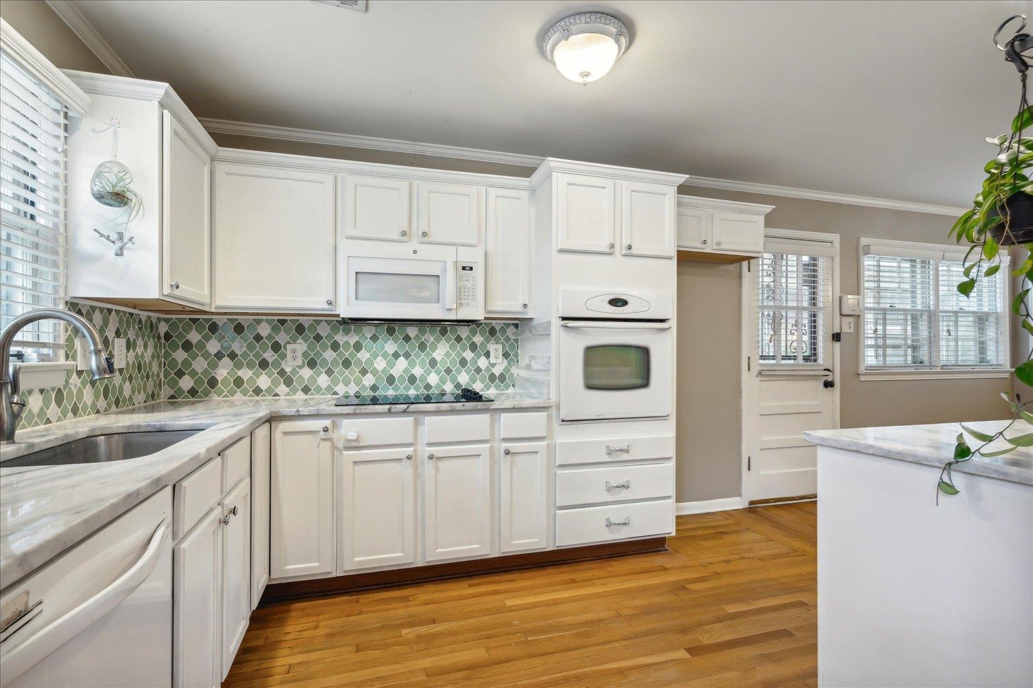 416 Fleda Road Memphis, TN 38120 - Photo 7 of 32 Kitchen with decorative backsplash, white cabinetry, light stone counters, light wood-type flooring, and white appliances