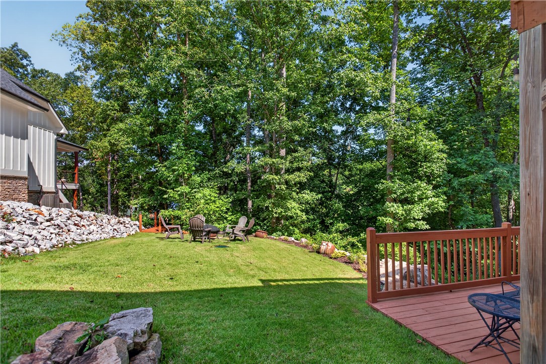 321 High Hampton Road Salem, SC 29676 - Photo 36 of 46 A wooden deck overlooks a level grassy lawn bordered by mature trees and stone retaining walls.