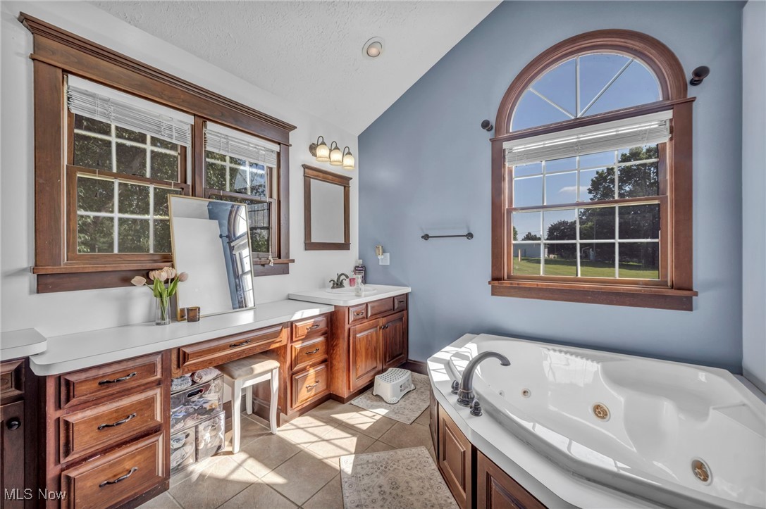 9827 Akron Road Rittman, OH 44270 - Photo 21 of 47 Full bath featuring vaulted ceiling, vanity, a jetted tub, tile patterned floors, and a textured ceiling
